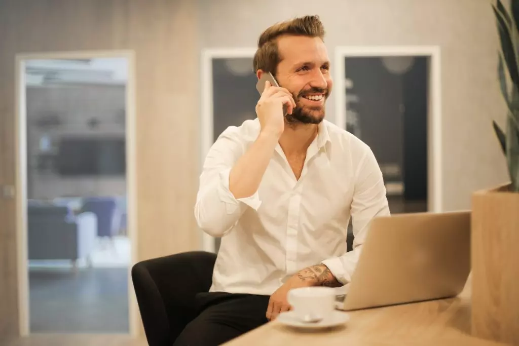 Hombre sonriendo mientras utiliza el teléfono sentado en una silla negra