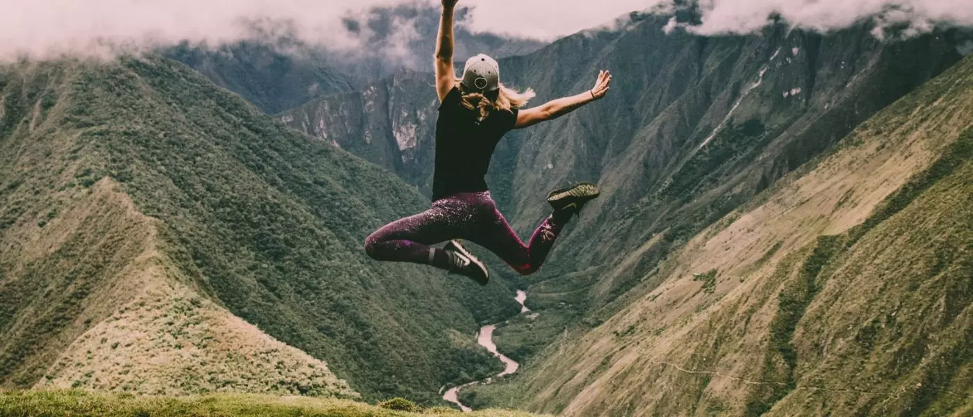 Mujer saltando en montaña con pastos verdes