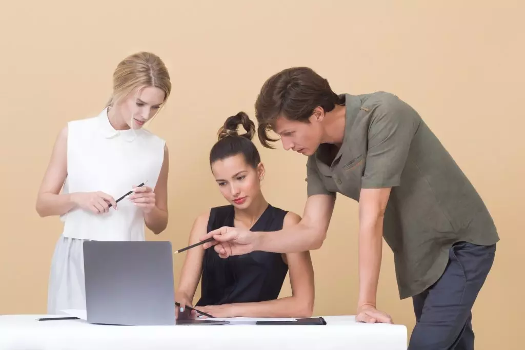 Hombre señalando una notebook enseñando algo a dos mujeres